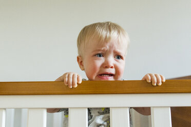 Cute baby boy looking away while crying in crib at home - CAVF51366