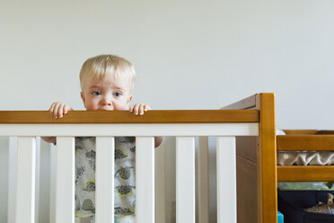 Niedlicher Babyjunge beißt in ein Holzgeländer, während er in einem Kinderbett zu Hause steht - CAVF51368