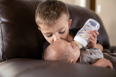 Junge füttert seinen Bruder mit Milch aus der Babyflasche und küsst ihn zu Hause - CAVF51375