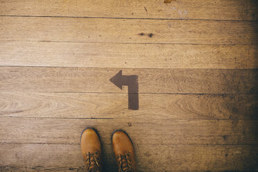 Low section of woman wearing shoes while standing by arrow symbol on wooden floor - CAVF51379