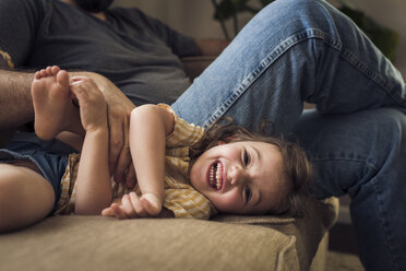 Porträt eines fröhlichen Mädchens mit Vater, das zu Hause auf dem Sofa spielt - CAVF51419