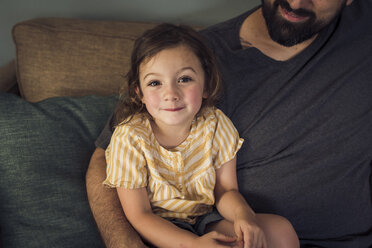 Hochformatiges Porträt eines Mädchens, das mit seinem Vater zu Hause auf dem Sofa sitzt - CAVF51420