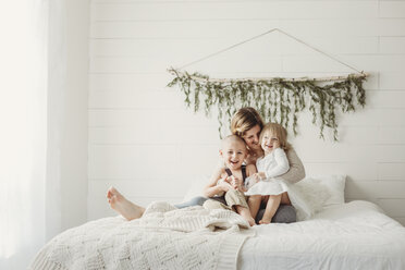 Glückliche Mutter mit Kindern, die zu Hause auf dem Bett sitzen - CAVF51446