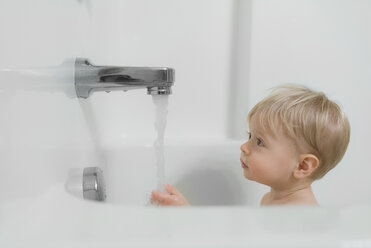 Niedlicher Junge schaut auf Wasser, das aus dem Wasserhahn im Badezimmer läuft - CAVF51451