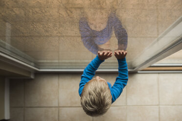 High angle view of baby boy looking through window while standing at home - CAVF51452