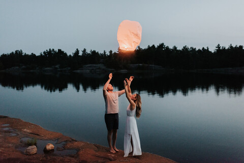 Paar lässt Himmelslaternen am See los, Algonquin Park, Kanada, lizenzfreies Stockfoto