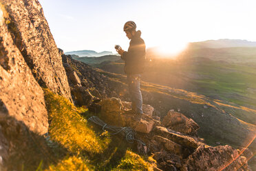 Pensive hiker using smart phone on mountain peak during sunrise at
