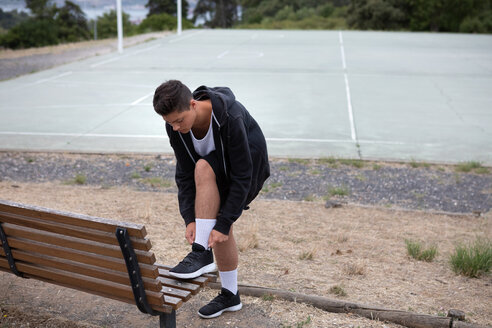 Männlicher jugendlicher Basketballspieler, der seine Turnschuhe am Basketballplatz befestigt - CUF46444