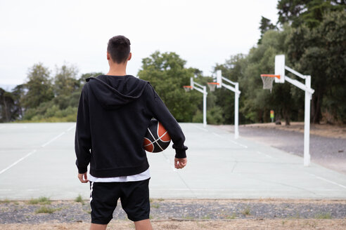 Männlicher jugendlicher Basketballspieler, der auf den Basketballplatz blickt, Rückansicht - CUF46445