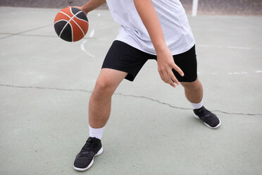Männlicher jugendlicher Basketballspieler, der auf dem Platz Basketball spielt, Taille nach unten - CUF46450