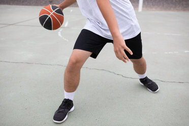 Male teenage basketball player playing basketball on court, waist down - CUF46450