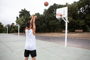 Male teenage basketball player throwing ball toward basketball hoop - CUF46451