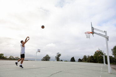 Male teenage basketball player throwing ball toward basketball hoop - CUF46453