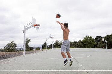 Male teenage basketball player jumping and throwing ball toward basketball hoop - CUF46458