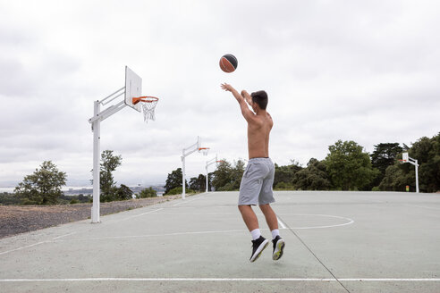 Männlicher jugendlicher Basketballspieler, der springt und den Ball in Richtung Basketballkorb wirft - CUF46458