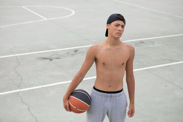 Männlicher jugendlicher Basketballspieler mit Ball auf dem Basketballplatz, Porträt - CUF46459