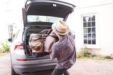 Young man in trilby removing luggage from car boot outside hotel, rear view - CUF46562