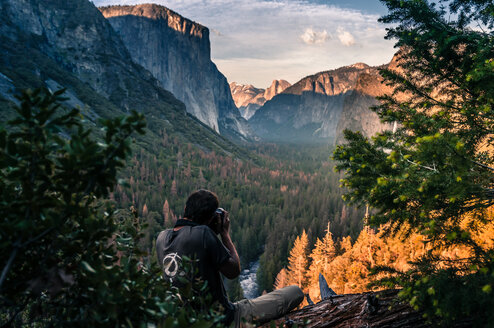 Rock climber taking photograph of mountain ranges, Yosemite National Park, California, USA - ISF20025