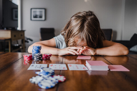 Girl playing cards at table with head down stock photo