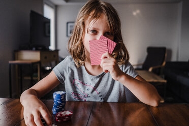 Girl hiding behind playing cards with gambling chips at table, portrait - ISF20039