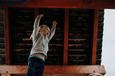 Girl jumping with arms raised on playground platform - ISF20065