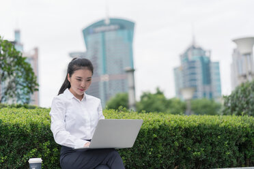 Young businesswoman typing on laptop in city financial district, Shanghai, China - ISF20066