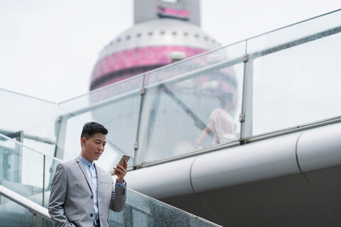 Junger Geschäftsmann, der auf einer Treppe in der Stadt auf sein Smartphone schaut, Shanghai, China, lizenzfreies Stockfoto