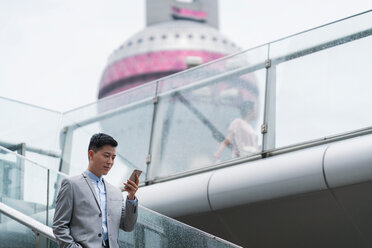 Junger Geschäftsmann, der auf einer Treppe in der Stadt auf sein Smartphone schaut, Shanghai, China - ISF20070