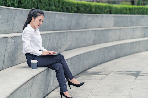 Junge Geschäftsfrau tippt auf einem Laptop auf einem Stadtsitz, Shanghai, China, lizenzfreies Stockfoto