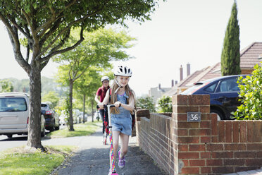 Happy girl riding scooter on neighborhood sidewalk - CAIF22185