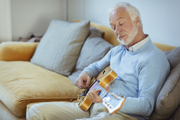 Active senior man playing guitar on living room sofa - CAIF22210