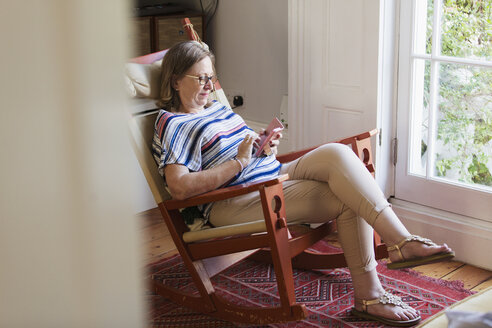 Ältere Frau, die im Schaukelstuhl mit ihrem Smartphone SMS schreibt - CAIF22219