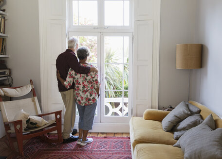 Liebevolles, gelassenes älteres Paar schaut aus dem Wohnzimmerfenster - CAIF22221