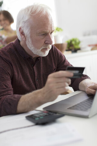 Konzentrierter älterer Mann mit Kreditkarte, der am Laptop Rechnungen bezahlt, lizenzfreies Stockfoto