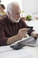 Konzentrierter älterer Mann mit Kreditkarte, der am Laptop Rechnungen bezahlt - CAIF22224