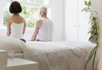 Thoughtful senior couple sitting on bed looking out window - CAIF22225