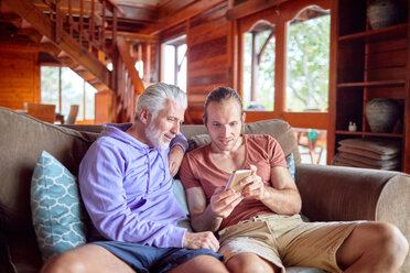 Father and son using smart phone on cabin sofa - CAIF22240