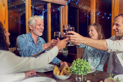 Freunde feiern, trinken Rotwein und genießen das Abendessen in der Hütte, lizenzfreies Stockfoto