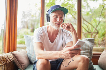 Mann mit Kopfhörern und mp3-Player beim Musikhören im Wohnzimmer - CAIF22245