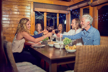 Freunde stoßen mit Rotweingläsern an und genießen das Abendessen am Esstisch der Hütte - CAIF22249