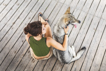 Young woman sitting besides her dog on plank floor, top view - WPEF01075