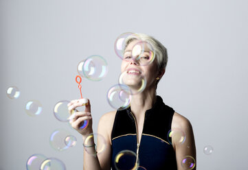 Porträt einer lächelnden Frau, die Seifenblasen beobachtet - FLLF00043