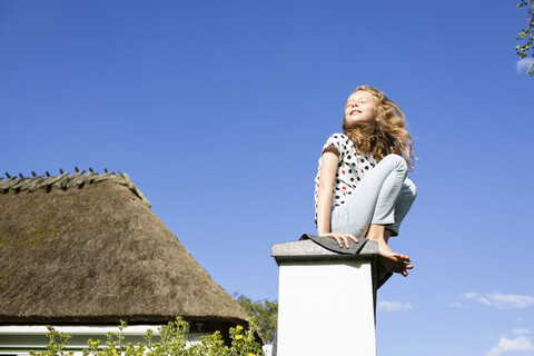 Mädchen sitzt auf einer Mauer unter blauem Himmel, lizenzfreies Stockfoto