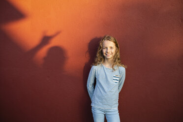 Porträt eines lächelnden Mädchens vor einer roten Wand mit Schatten - OJF00266