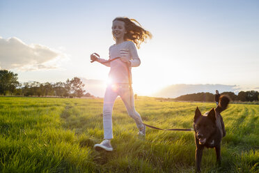 Mädchen mit Hund läuft bei Sonnenuntergang über ein Feld - OJF00270