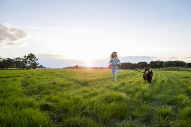 Mädchen mit Hund läuft bei Sonnenuntergang über ein Feld - OJF00271