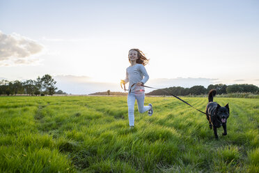 Girl with a dog running over a field at sunset - OJF00272