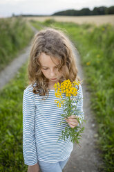Girl standing on field path holding a wild flower - OJF00275