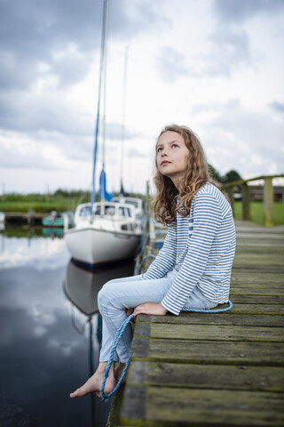 Girl sitting on a jetty in a small harbor stock photo
