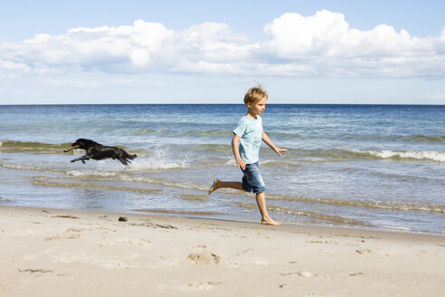 Junge mit Hund läuft am Strand - OJF00279